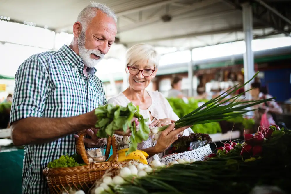 a senior couple picking out vegetables outdoors at a farmers market