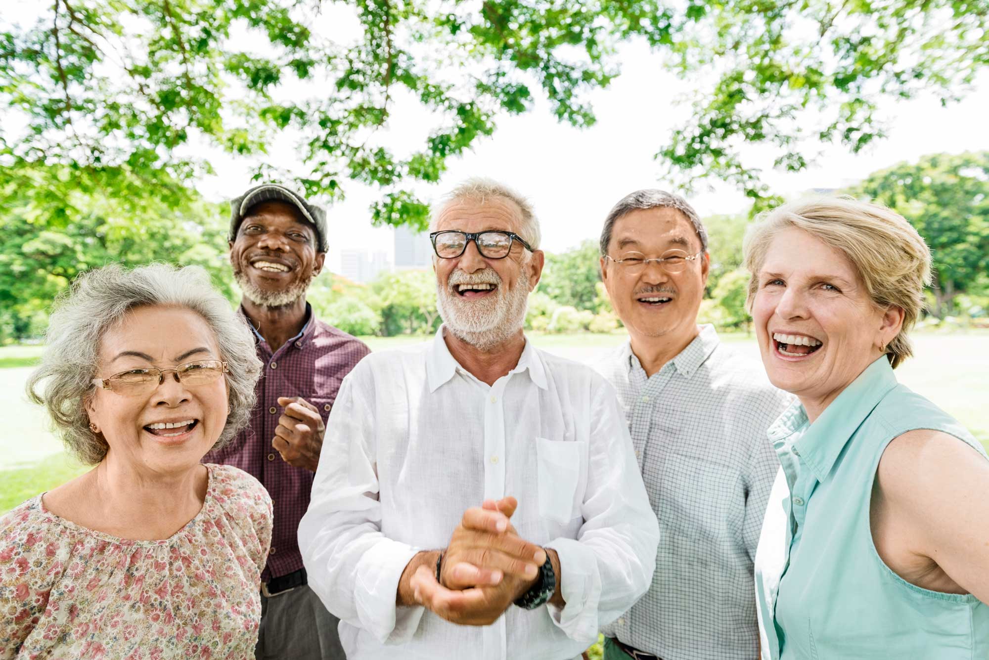a group of seniors laughing and smiling while outside under the shade of a tree